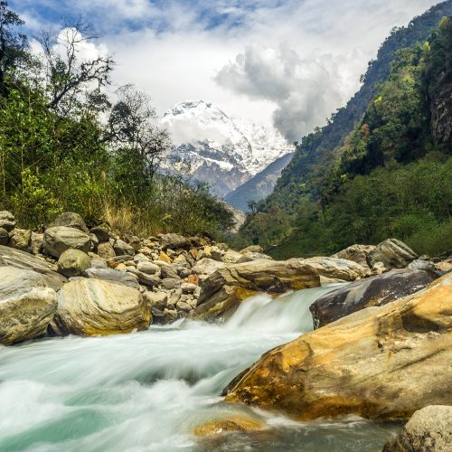 A vertical shot of a rapid river crashing on the rocks with mountains in the background